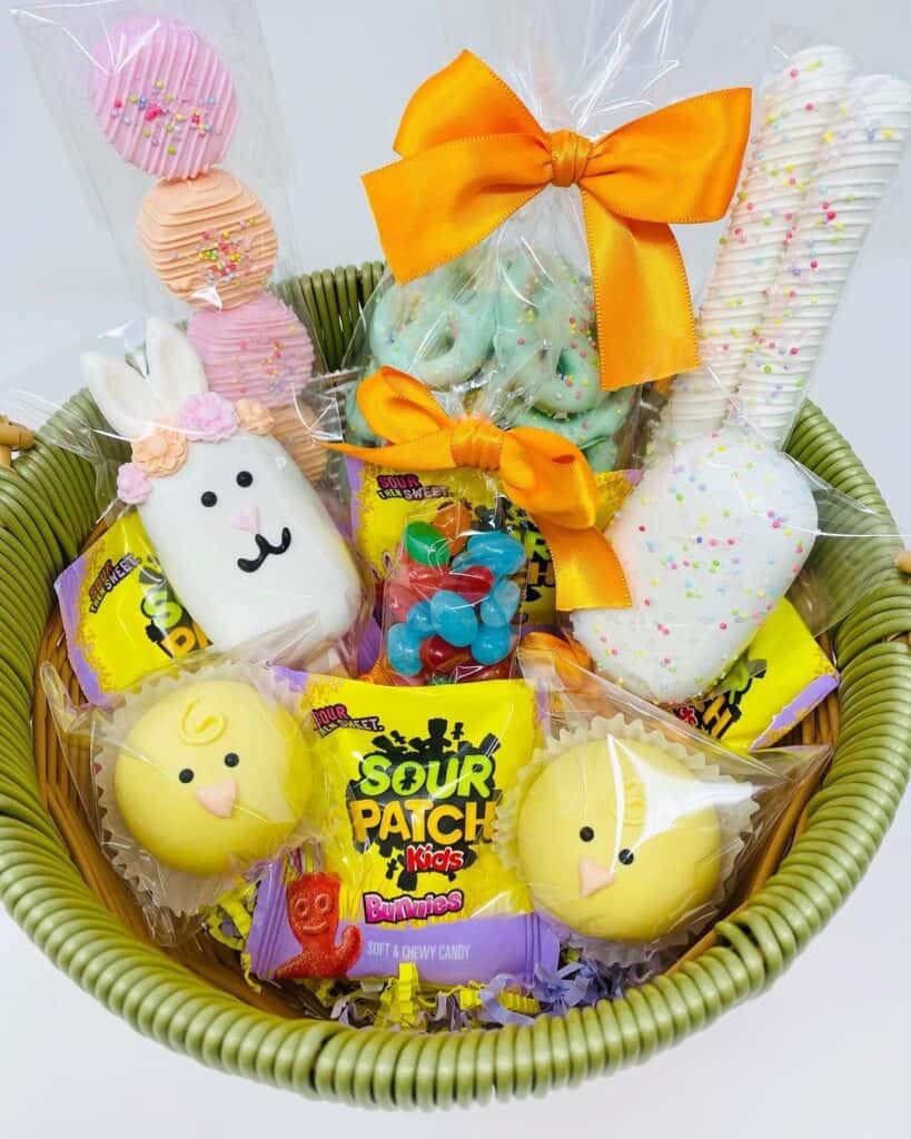 Easter basket filled with candies like sour patch, marshmallow peeps, macaroons, chocolate covered pretzels, jelly beans. Plastic wrap and tied with an orange bow